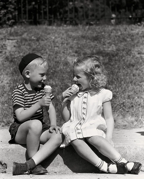 Boy and girl sitting on curb, eating ice cream cones