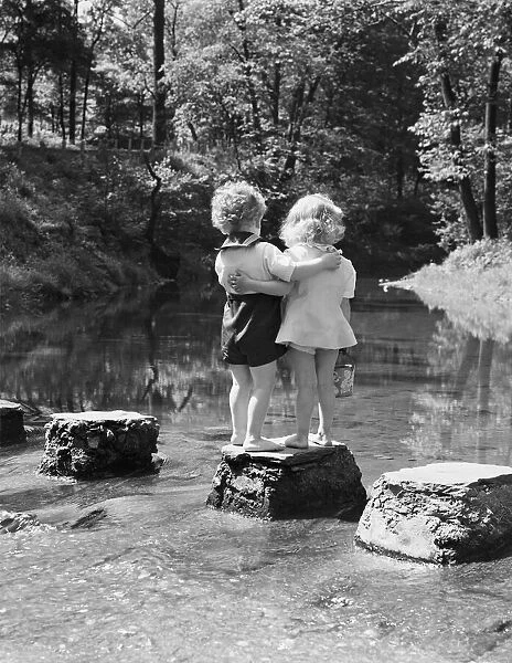 Boy and girl standing on rock path in stream, with arms around each other