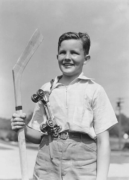 Boy holding hockey stick, metal roller skates hanging on his shoulder, smiling, portrait