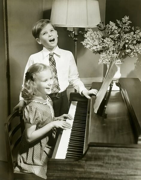Boy singing beside girl playing piano
