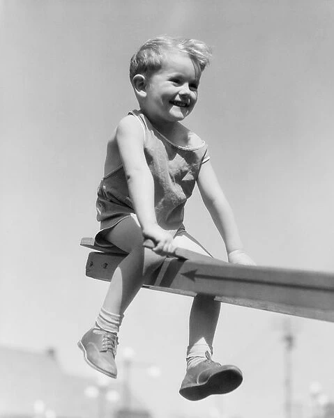 Boy sitting on see-saw in playground, legs dangling