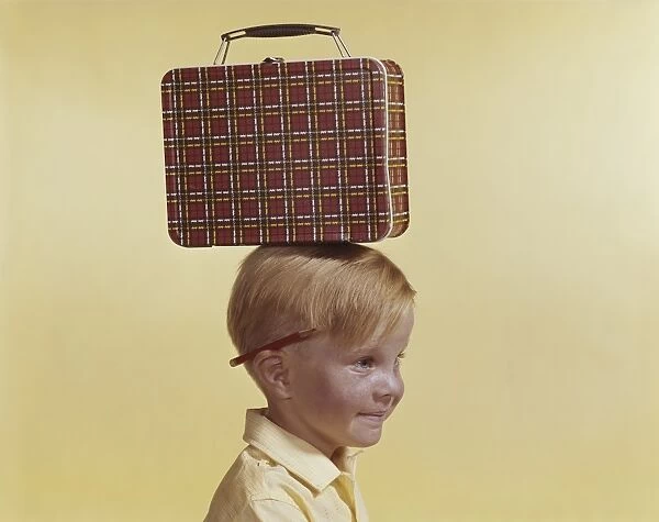 Boy with small luggage on his head against yellow background, close-up