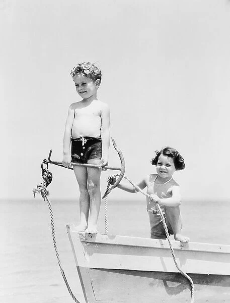 Boy standing on bow of row boat holding anchor, girl holding rope