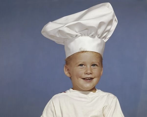Boy wearing chefs hat, smiling, close-up