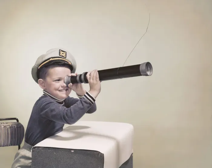 Framed Print : Boy wearing sailor hat looking through telescope, smiling Framed Print : Boy wearing sailor hat looking through telescope, smiling