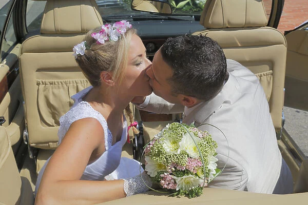 Bride and groom kissing in the back seat of an open car, convertible
