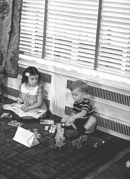 Brother (4-5) and sister (6-7) playing on floor in family room, (B&W)