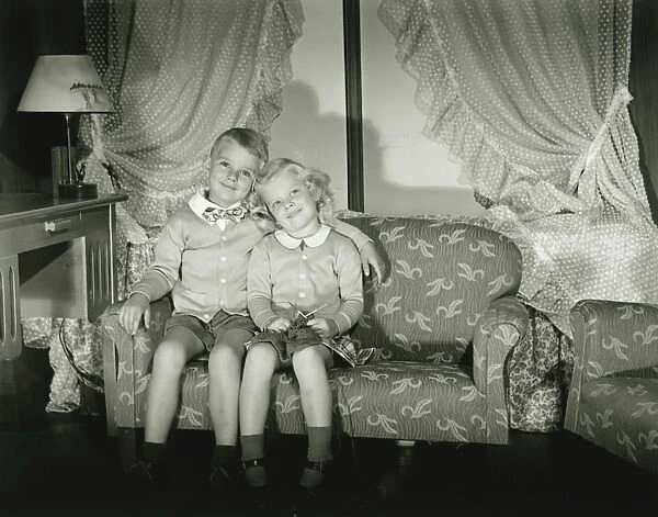 Brother and sister (4-5) posing in room, (B&W), portrait