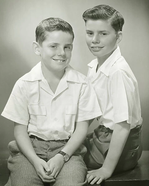 Brothers (8-9) (10-11) sitting in studio, smiling, (B&W), portrait