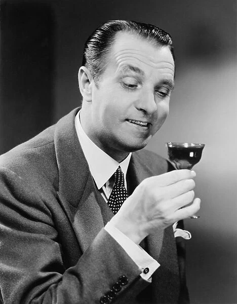 Businessman with glass of beverage, posing in studio, (B&W), close-up