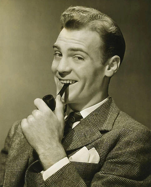 Businessman holding pipe in mouth, smiling, (B&W), portrait