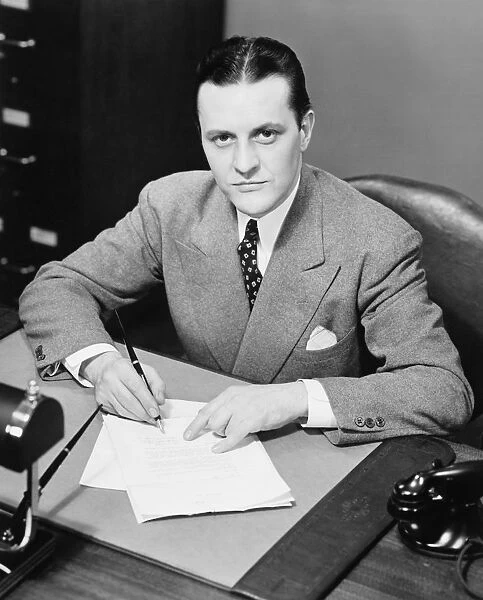 Businessman signing papers at desk in office, (B&W), portrait, elevated view