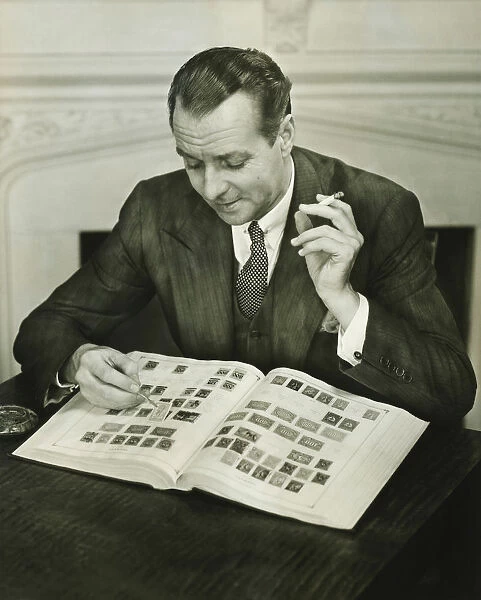 Businessman sitting at small table, with stamp album, (B&W)