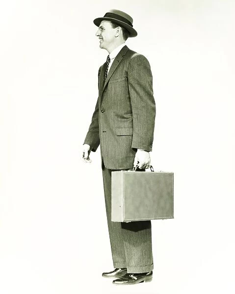 Businessman standing in studio, holding briefcase, (B&W)