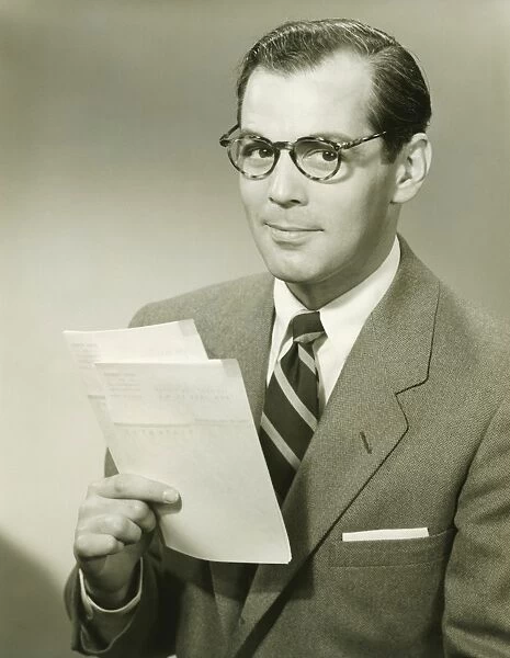 Businessman in studio holding papers, (B&W), portrait