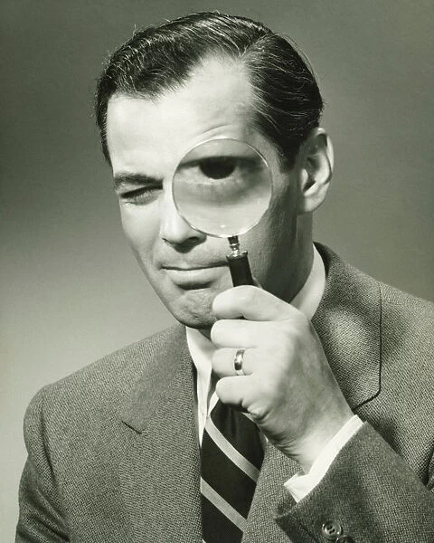 Businessman in full suit in studio looking through magnifying glass, (B&W), portrait