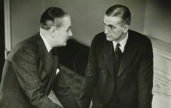 Two businessmen leaning on desk, talking, (B&W)