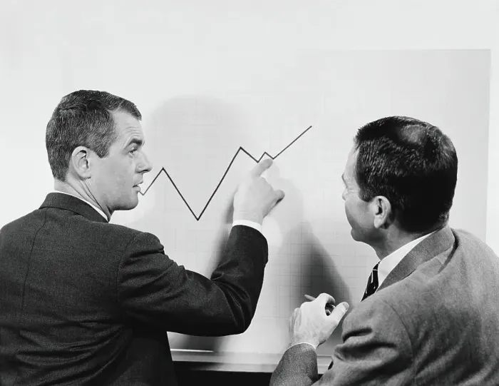Framed Print : Two businessmen standing in front of chart graphic, pointing to line, peaks and valleys showing growth Framed Print : Two businessmen standing in front of chart graphic, pointing to line, peaks and valleys showing growth