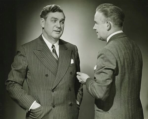 Two businessmen talking in studio, (B&W), portrait
