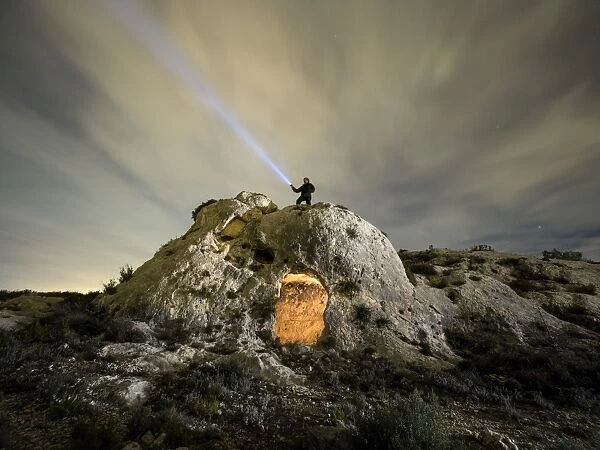 Cave excavated on the rock with a man on top, making signals with a flashlight