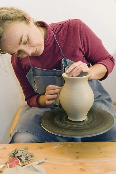 Ceramic artist working in her workshop with a potters wheel, polishing the surface of a pitcher, Geisenhausen, Bavaria, Germany, Europe
