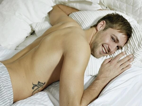 Charming bare chested man wearing pyjamas lying in bed, smiling