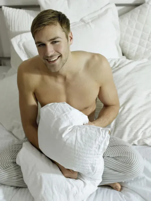 Framed Print : Charming bare chested man wearing pyjamas sitting on a bed, smiling Framed Print : Charming bare chested man wearing pyjamas sitting on a bed, smiling
