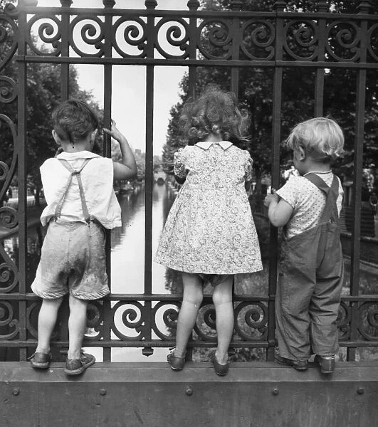 Three children peer through the fence on a bridge over one of Londons many canals