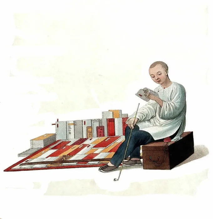 Framed Print : A Chinese bookseller sitting on a box in the street reading in front of his books, c. 1810, China, Historical, digitally restored reproduction from a 19th century original Framed Print : A Chinese bookseller sitting on a box in the street reading in front of his books, c. 1810, China, Historical, digitally restored reproduction from a 19th century original