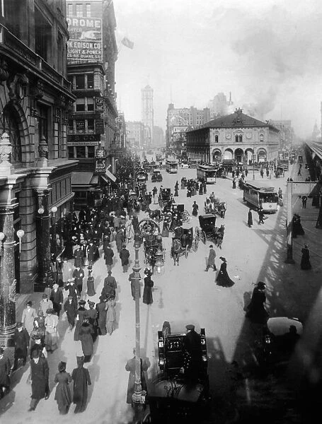 circa 1902: Crowds of people move through Herald Square on foot, in horse drawn carriages