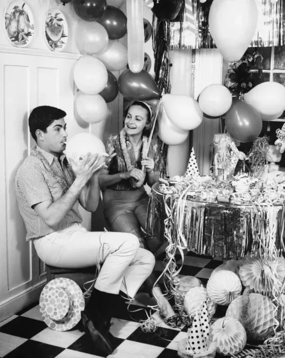Framed Print : Couple blowing up balloons in kitchen for party, (B&W) Framed Print : Couple blowing up balloons in kitchen for party, (B&W)