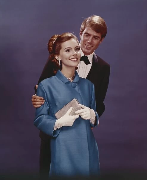 Couple in formal clothing standing against blue background, smiling