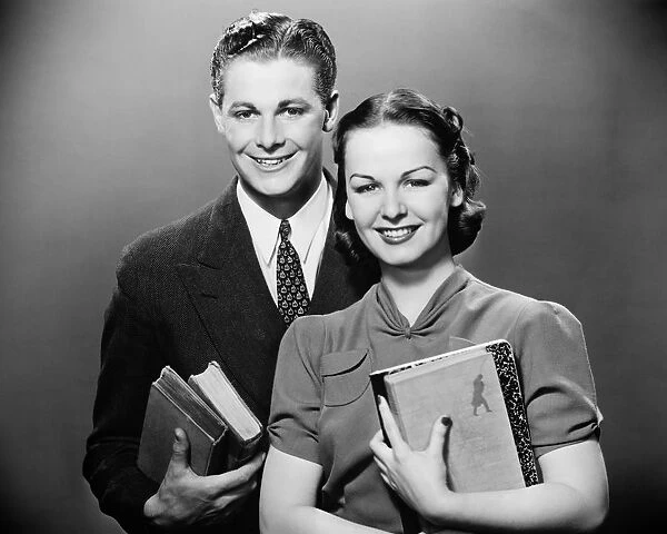 Couple holding books, posing in studio, (B&W), portrait