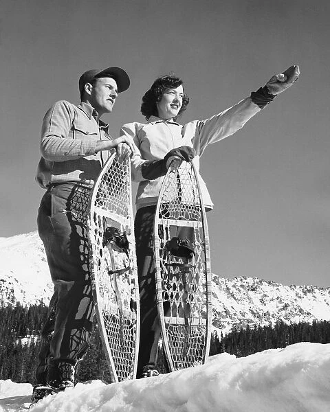 Couple holding snowshoes, woman pointing