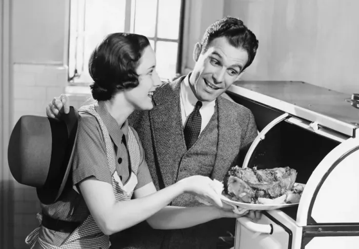 Framed Print : Couple in kitchen, wife taking roast from oven, (B&W) Framed Print : Couple in kitchen, wife taking roast from oven, (B&W)