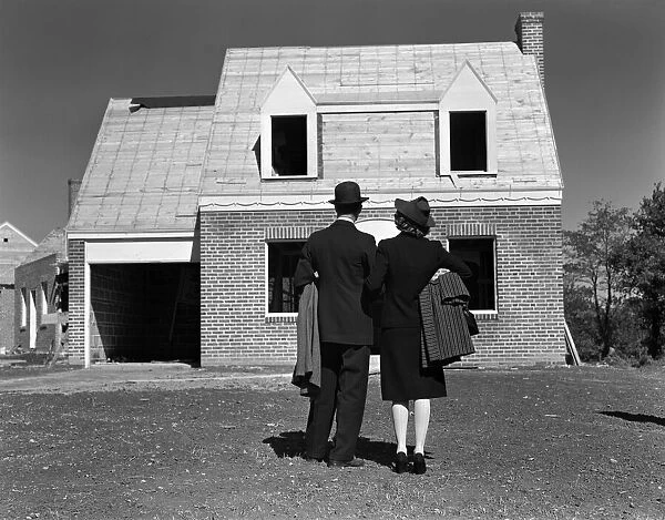 Couple looking at brick house under construction, rear view