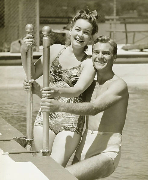 Couple standing at railings in pool, (B&W), portrait