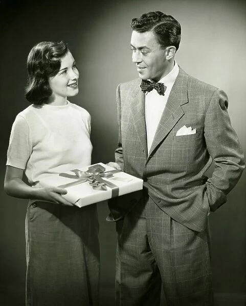 Couple standing in studio, woman holding present, (B&W)