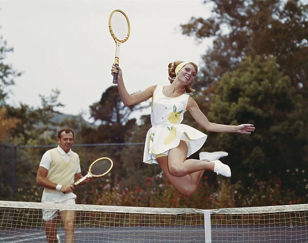 Couple on tennis court, woman jumping in foreground