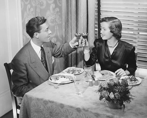 Couple toasting at dinner table, (B&W), elevated view