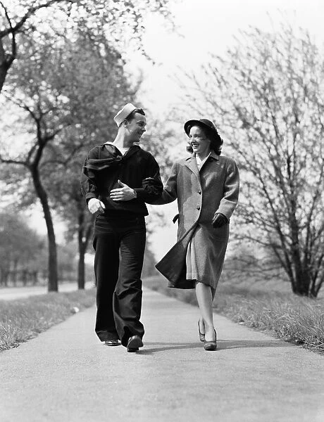 Couple walking arm in arm outdoors, man wearing naval sailor uniform, woman wearing coat