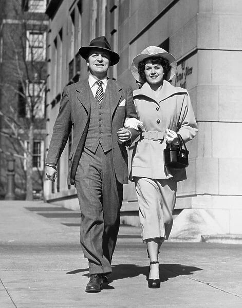 Couple walking arm in arm along sidewalk, portrait