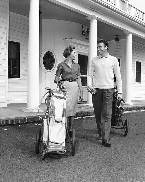 Couple walking with golf carts in front of clubhouse