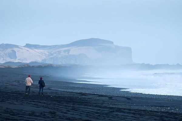 A couple are walking along the Viks black beach