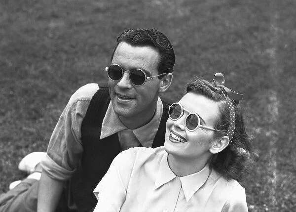 Couple wearing sunglasses sitting on grass, (B&W)