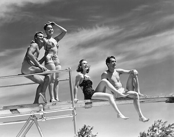 Two couples sitting on springboard, (B&W), low angle view
