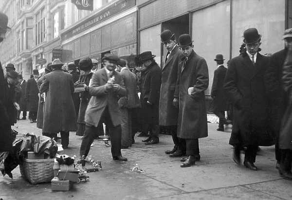 A crowd on a sidewalk observes street peddlers selling toys