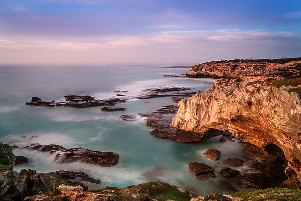 The dangerous and rugged coastline of Arniston where many shipwrecks have taken place with sunrise painting the cliff face and clouds with color. Arniston, Western Cape Province, South Africa