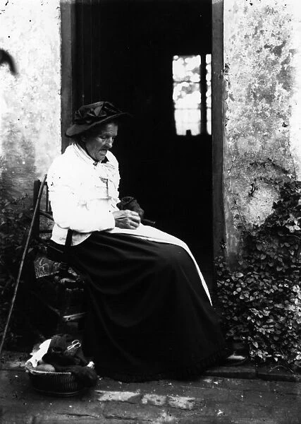 Darning. circa 1900: An old woman sits outside darning socks