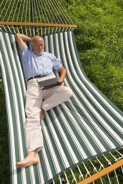 Elderly gentleman lying in a hammock with a netbook